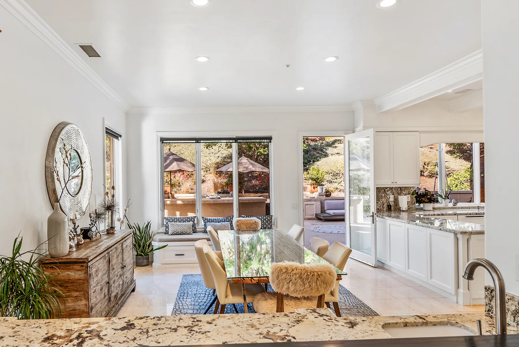A bright open-plan dining area and kitchen with large windows and a glass dining table.