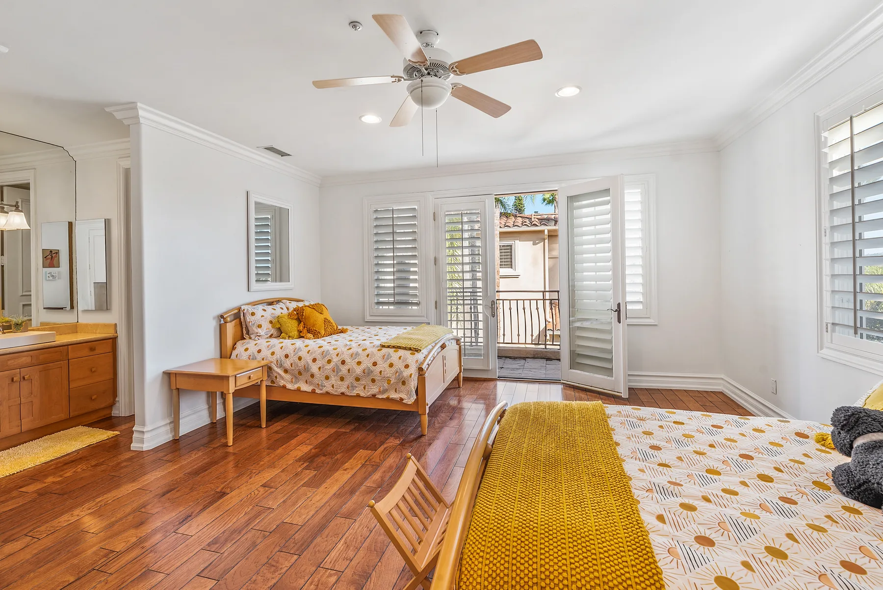 A bright bedroom with two beds, wood flooring, and open doors to a balcony.