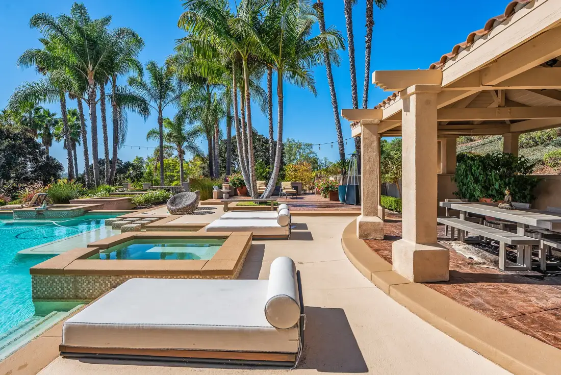 A sunny poolside patio with lounge seating and a covered dining area.
