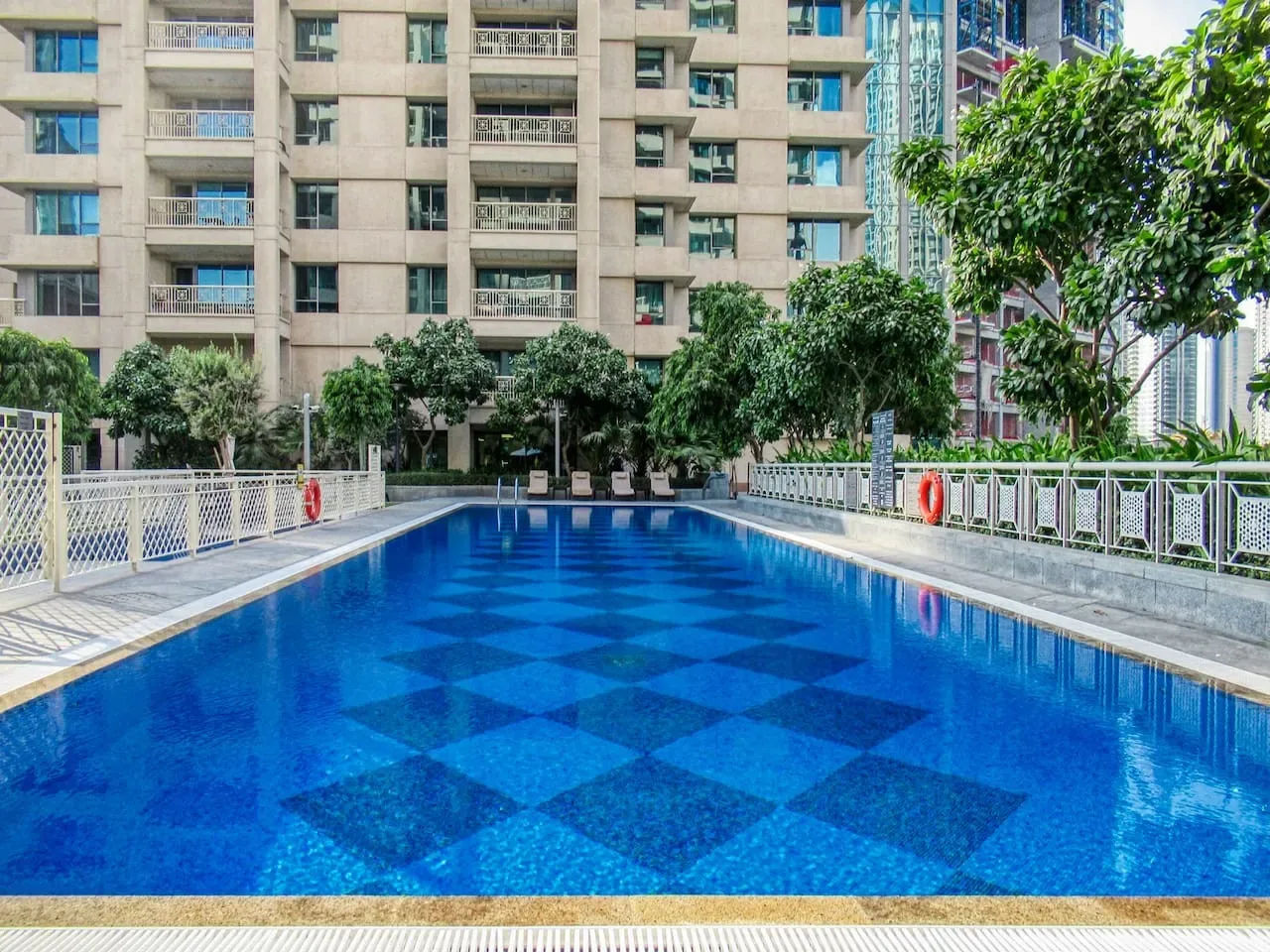 Una piscina al aire libre está junto a una terraza pavimentada y edificios de apartamentos.