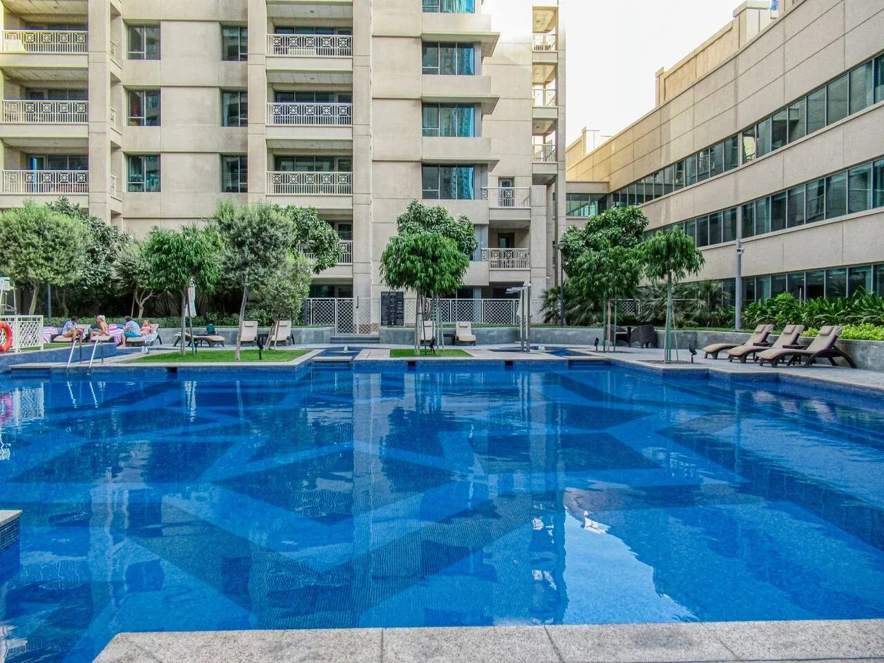 Una piscina al aire libre está entre edificios de varios pisos, con asientos junto al borde.