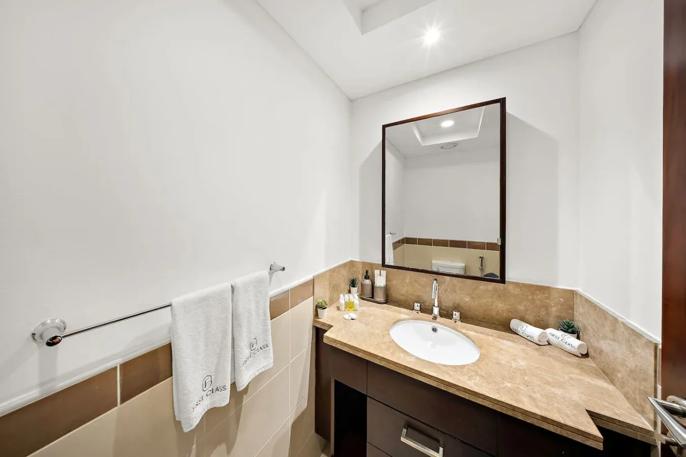 Un tocador de baño con lavabo y espejo junto a paredes revestidas de azulejos.