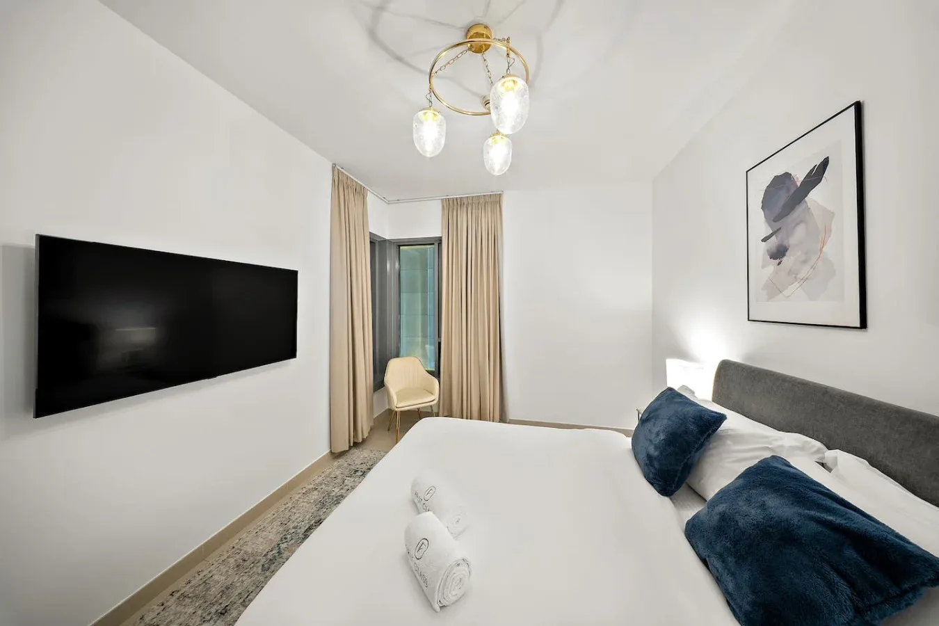 Un dormitorio con cama, televisor en la pared y una ventana con cortinas.