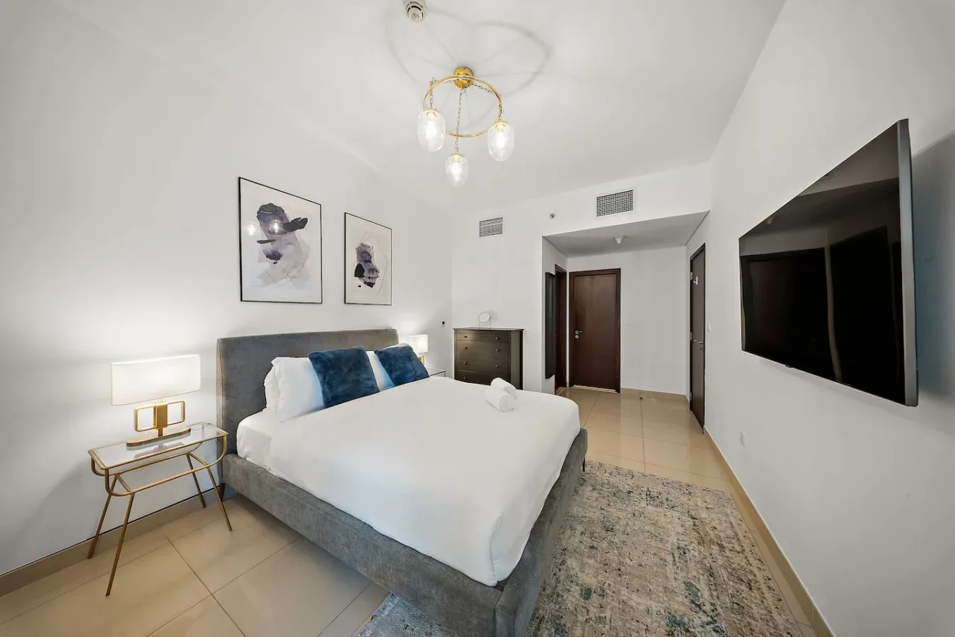 Un dormitorio luminoso con una cama tendida y un televisor montado en la pared.