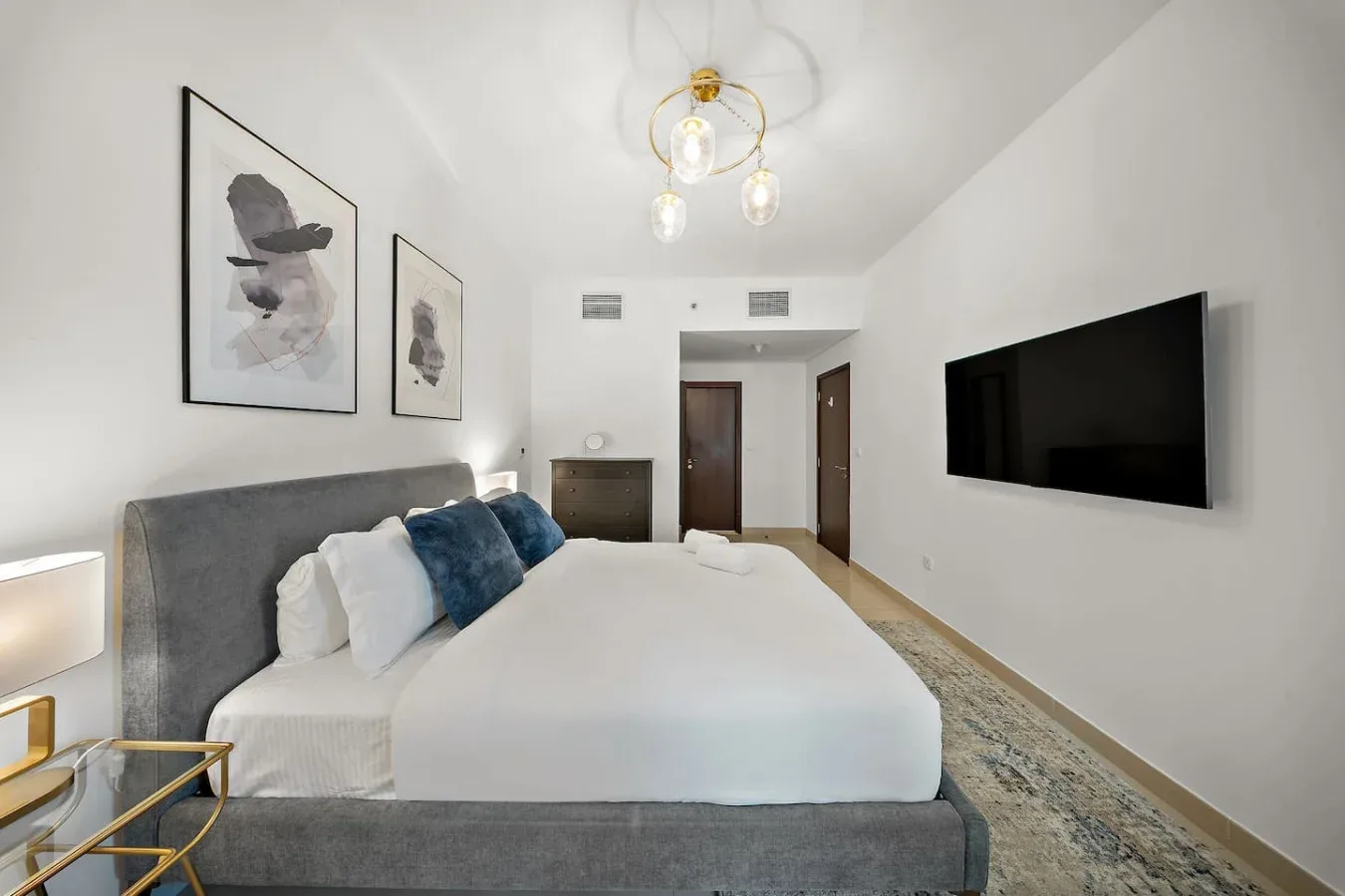 Un dormitorio luminoso con una cama bien hecha y un televisor montado en la pared.