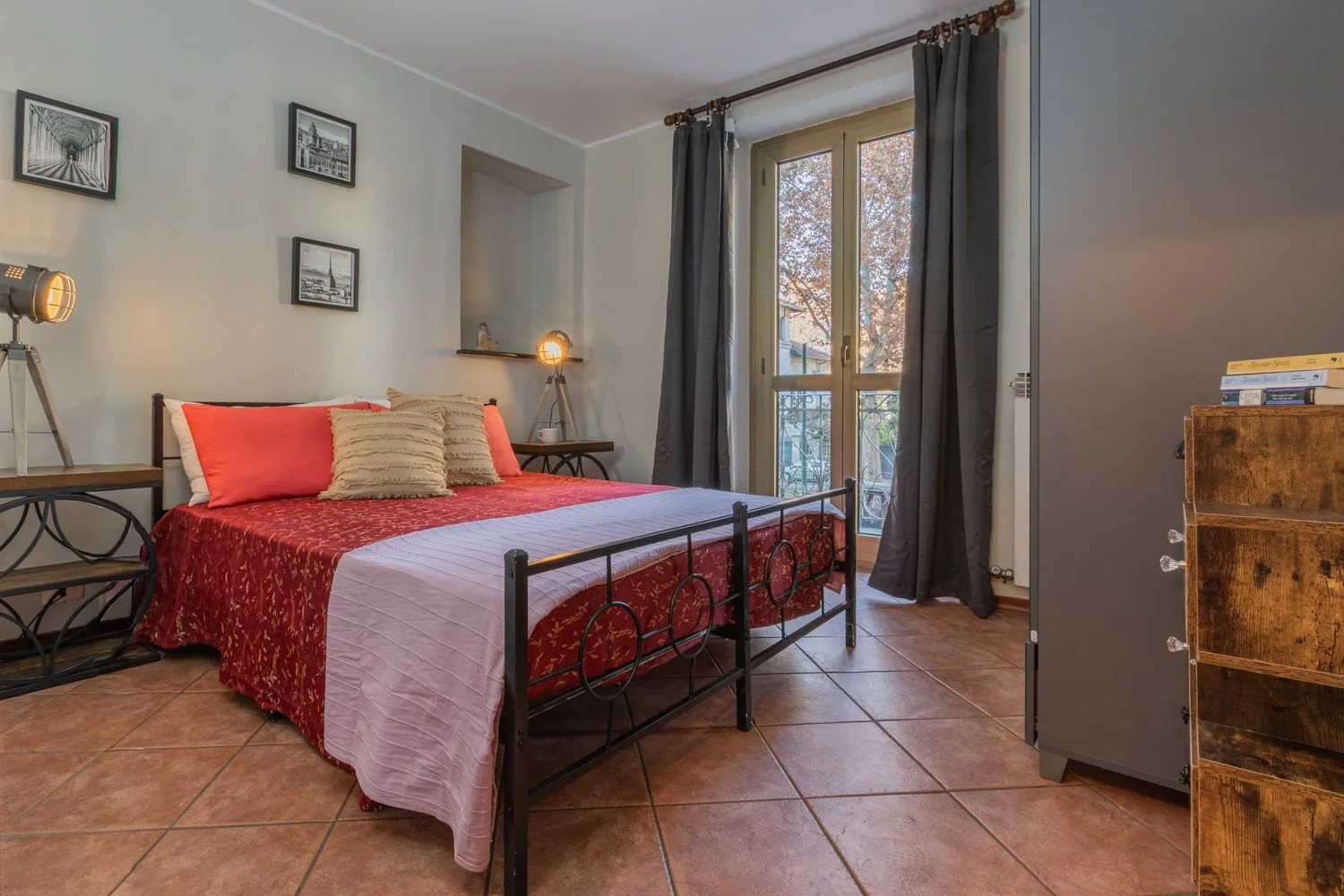 A bedroom with a bed, bedside tables, and a tall window with dark curtains.