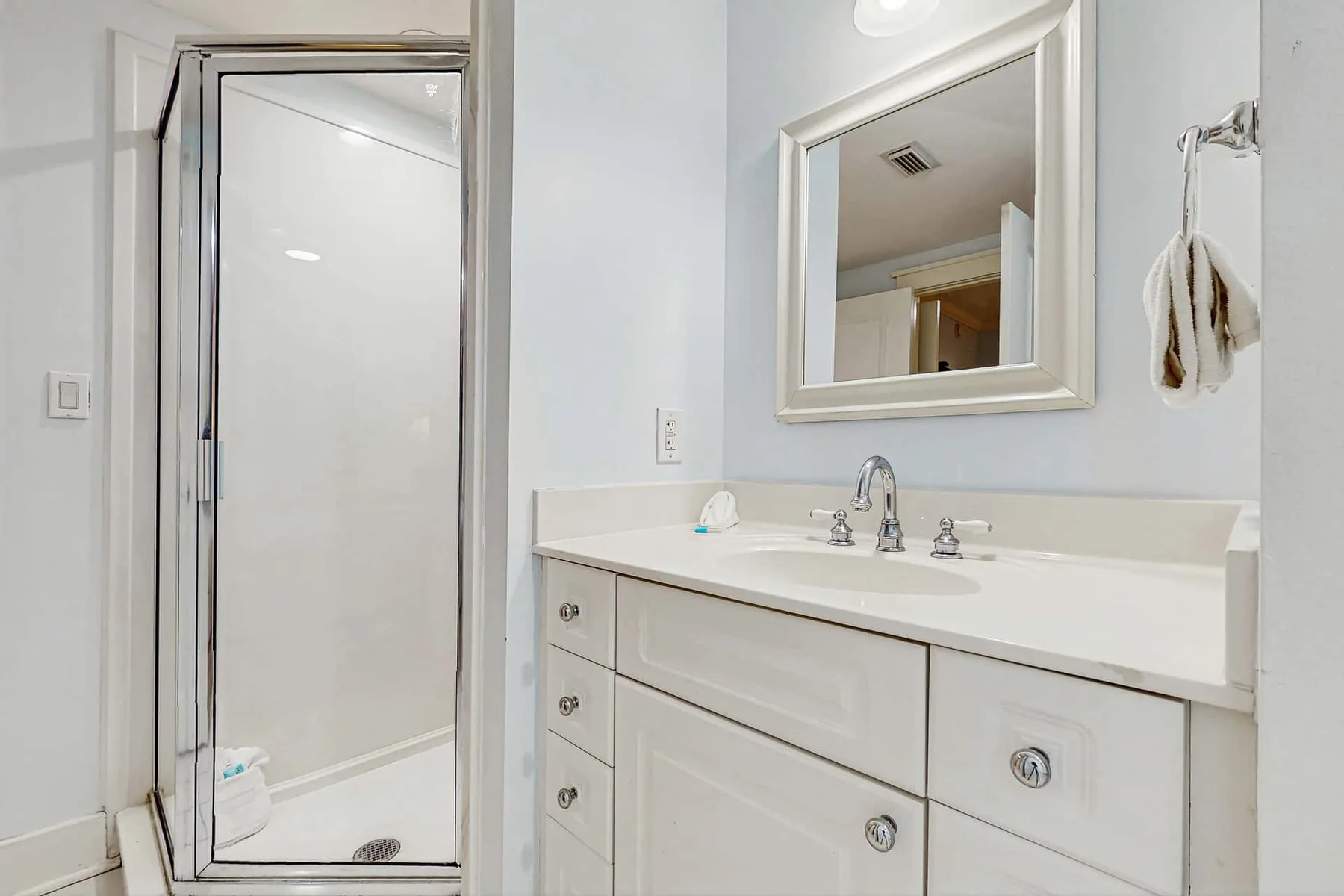 A bathroom vanity with a sink and mirror beside a glass shower.