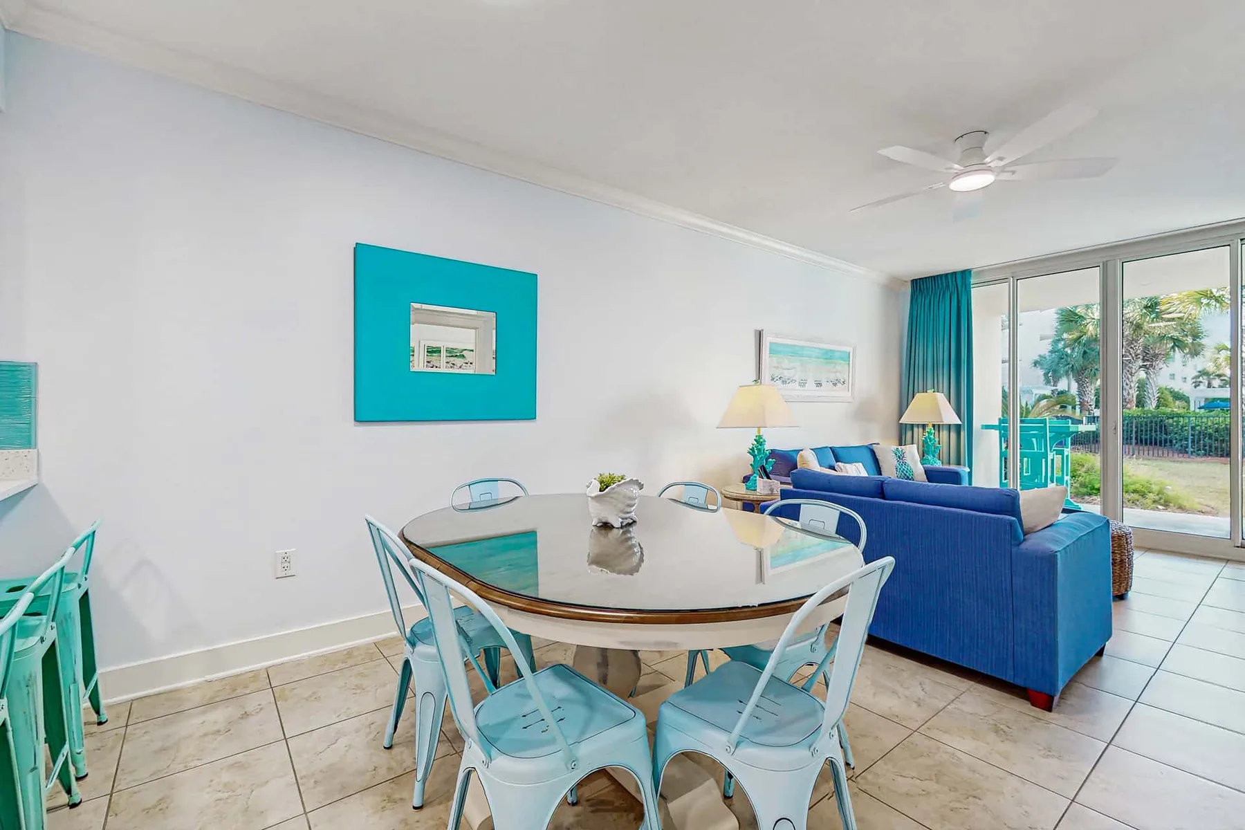 A dining area opens into a living space with blue seating and sliding glass doors.