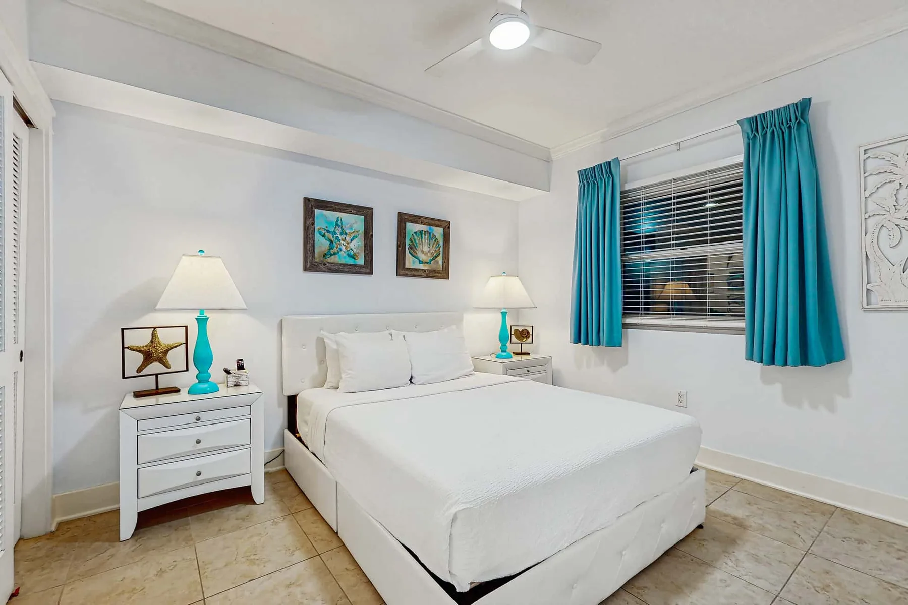 Bedroom with a white bed and turquoise curtains beside the window.