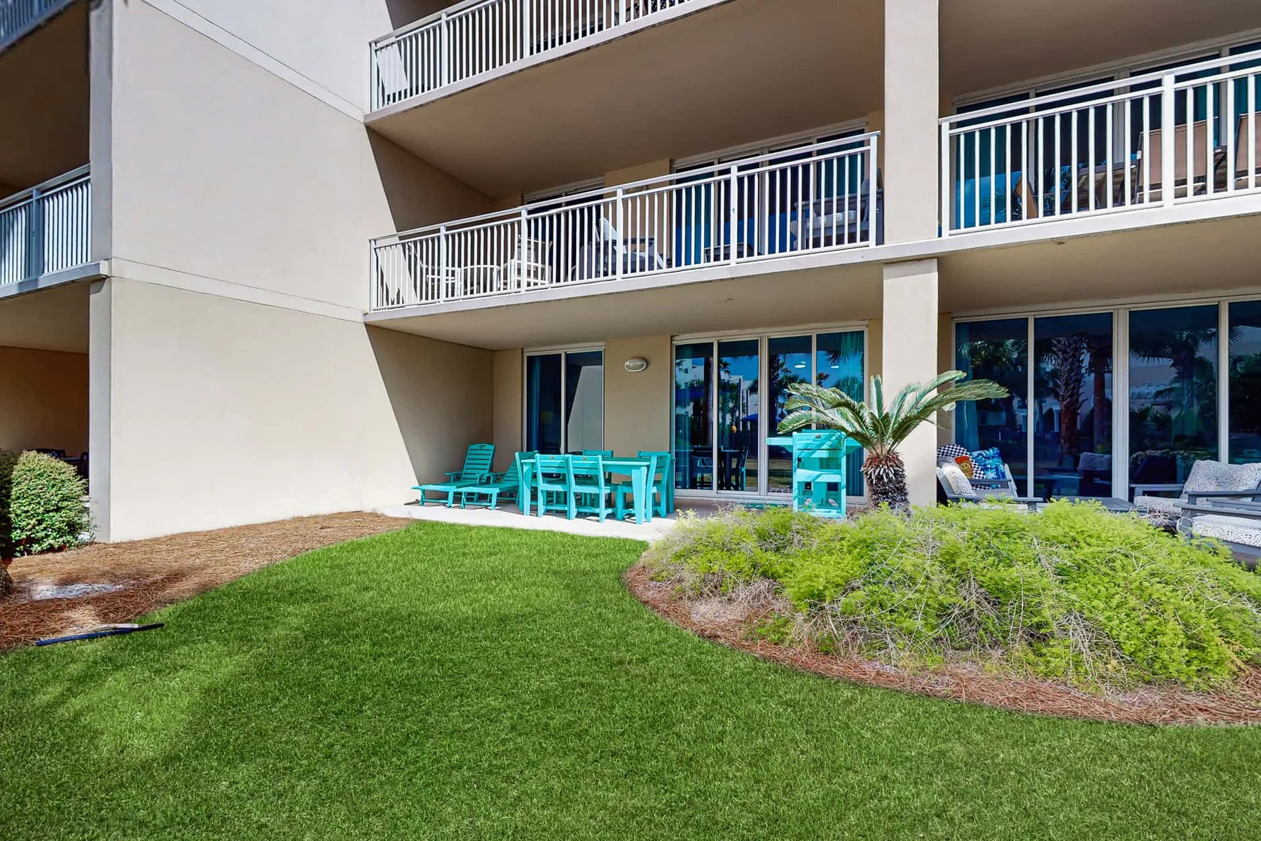 An outdoor lawn borders a building with balconies and turquoise patio seating.