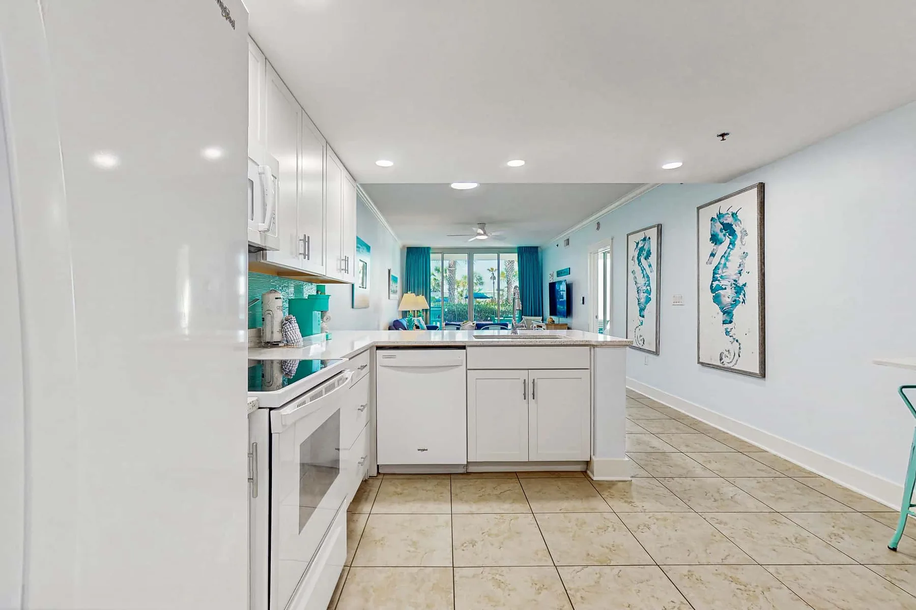 A bright kitchen with white cabinets and a long counter opens into a living area.