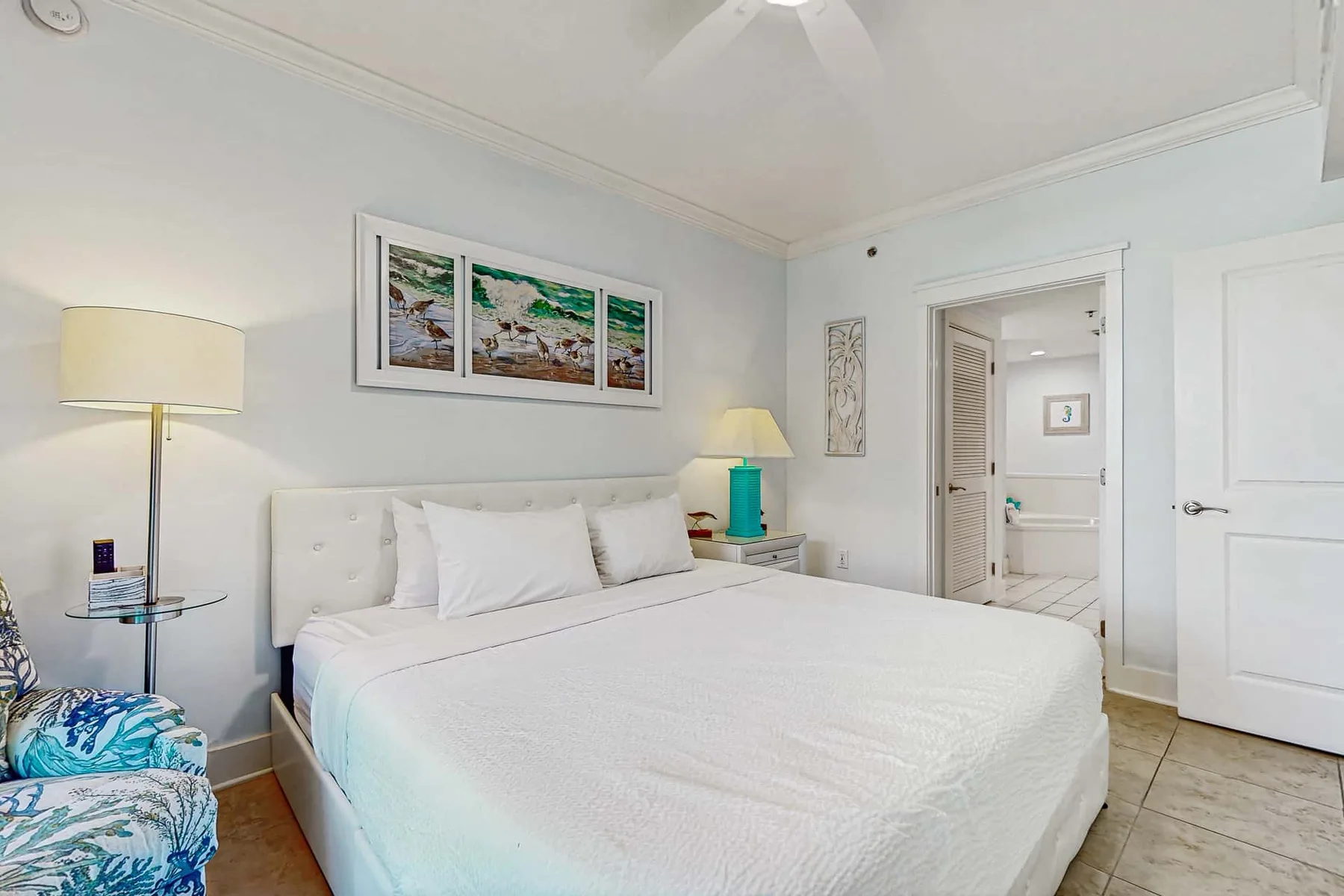 A bright bedroom with a white bed and framed artwork on the wall.
