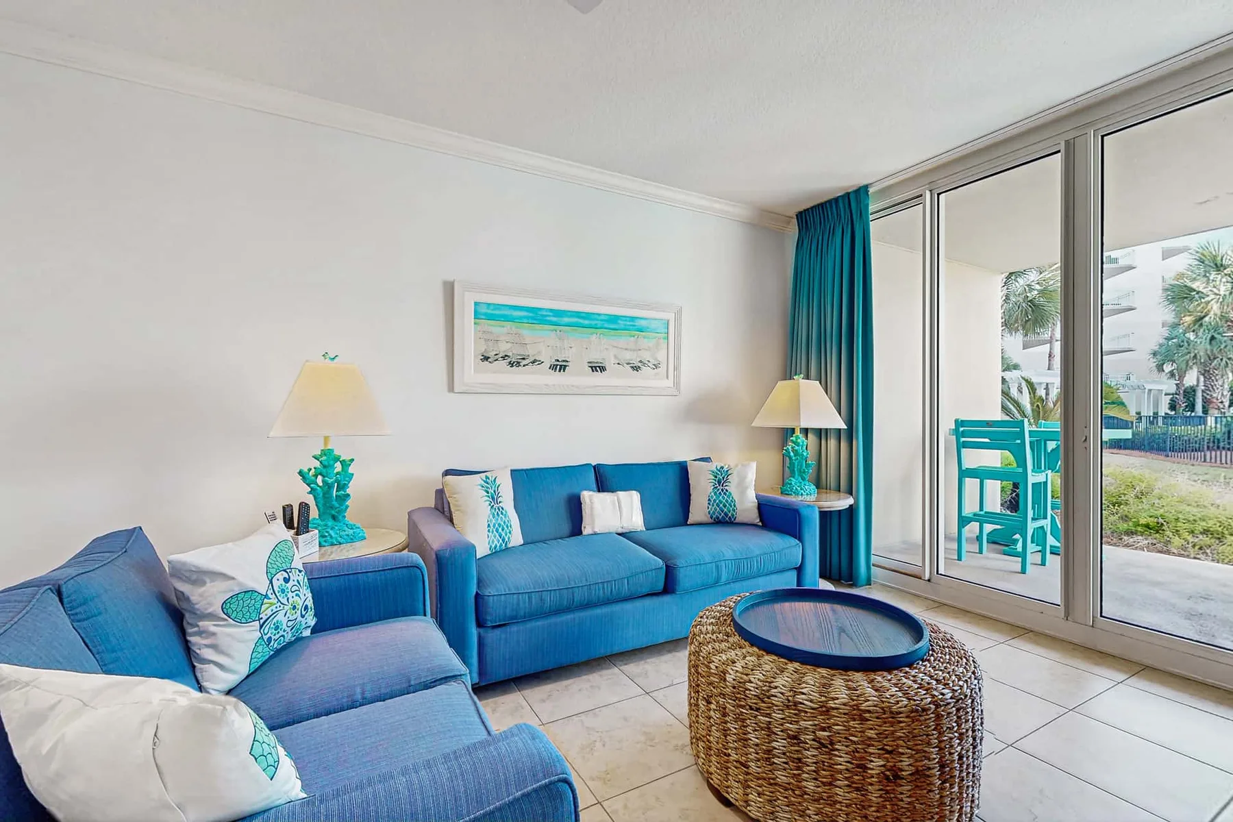 A bright living room with blue seating, a round woven table, and sliding glass doors.