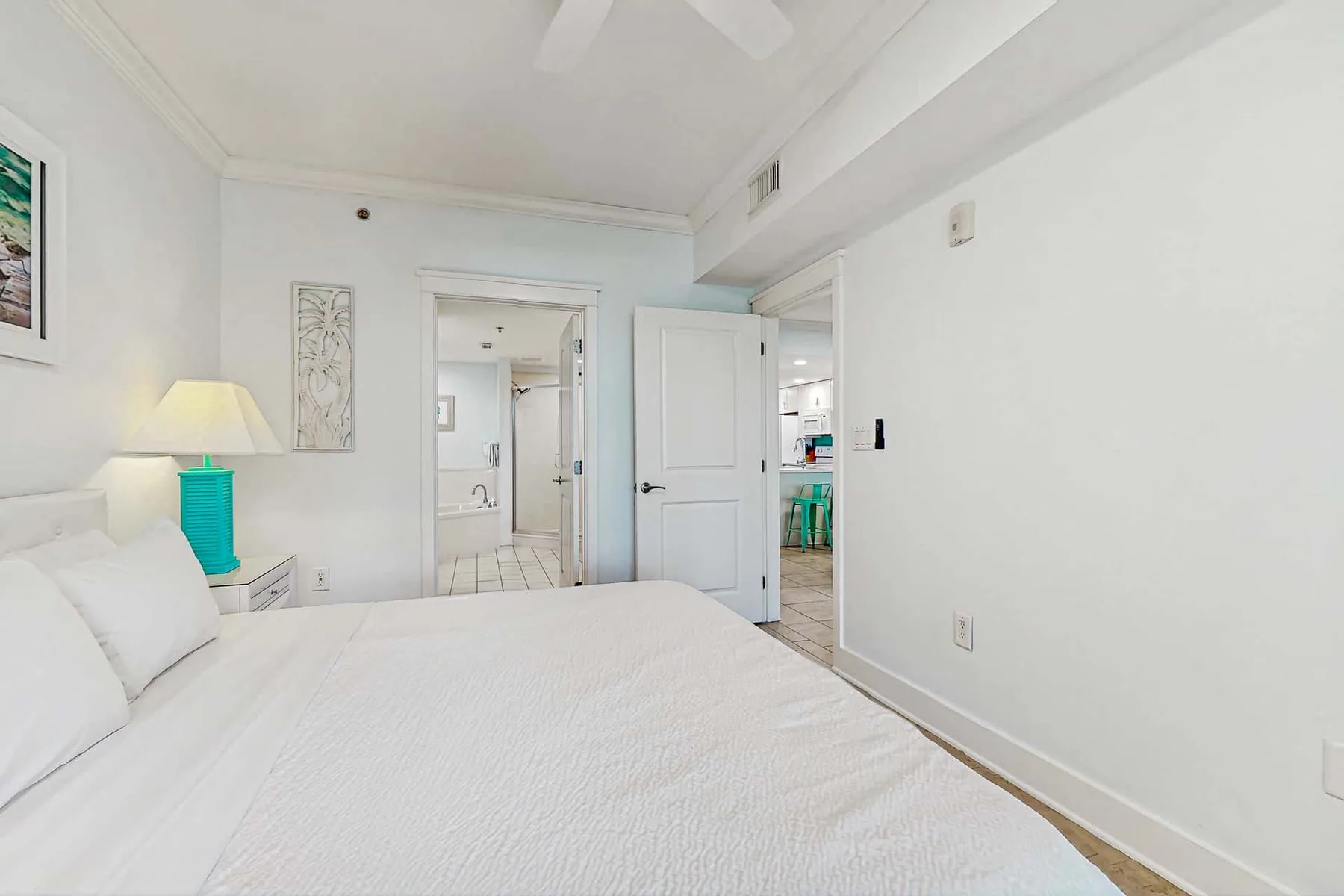 A bright bedroom with a white bed and open doors leading to adjoining rooms.