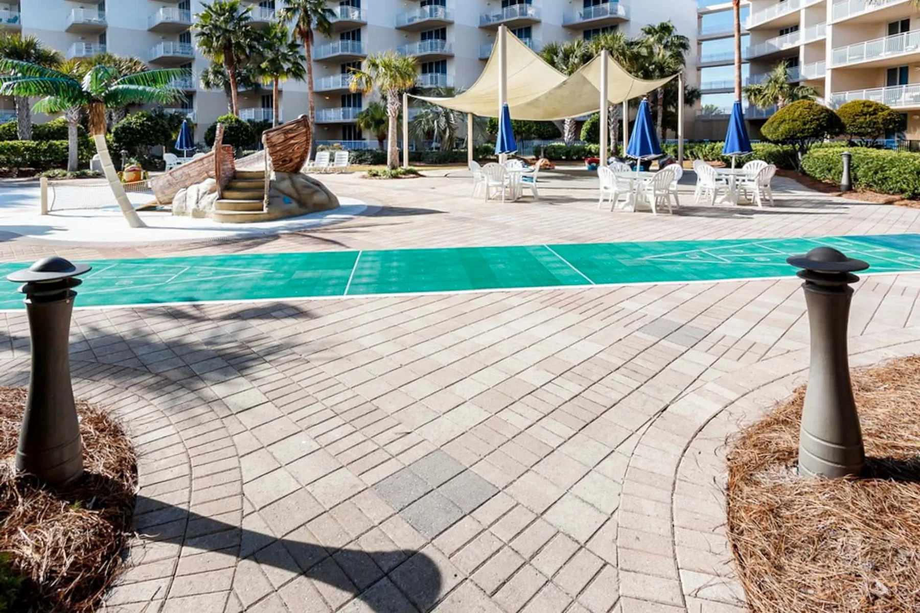 Outdoor pool area with a shallow splash feature, shaded seating, and surrounding buildings.