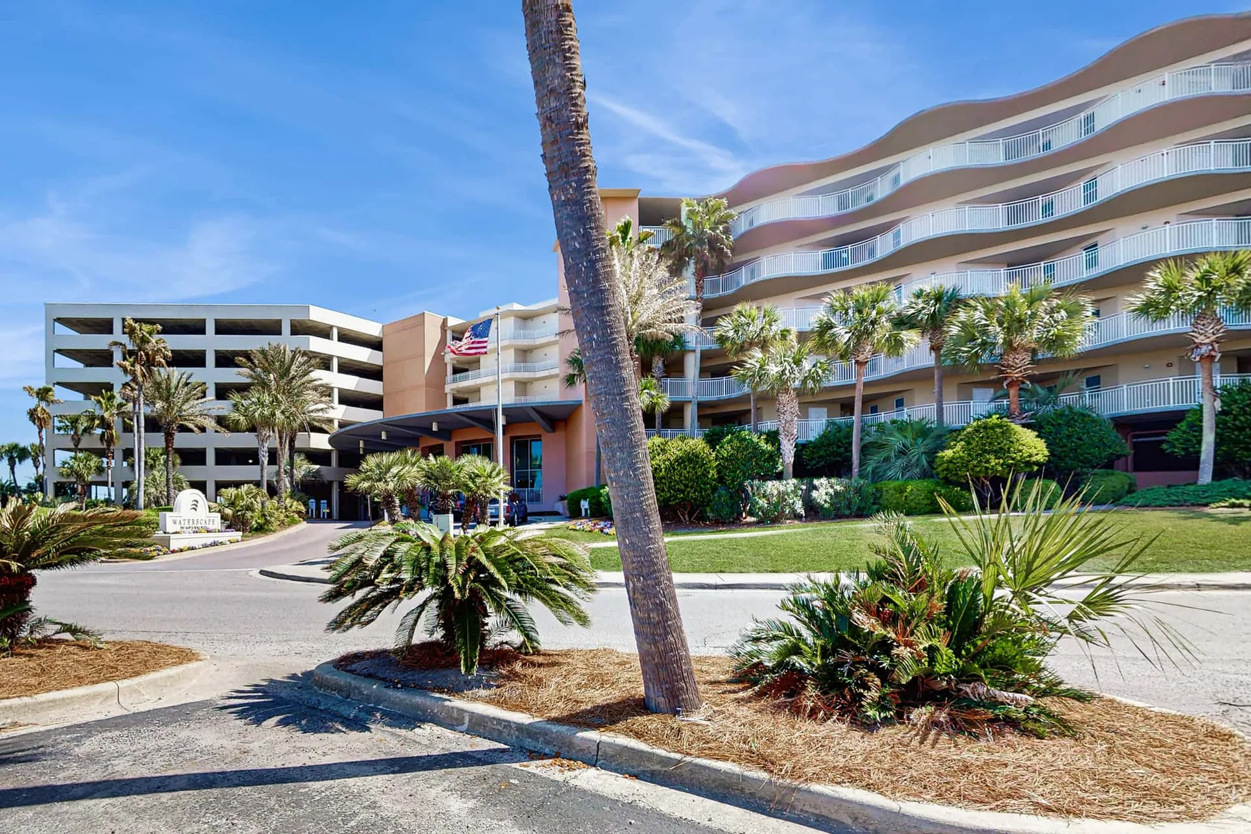 A curved multi-story building stands behind a landscaped driveway and palm trees.