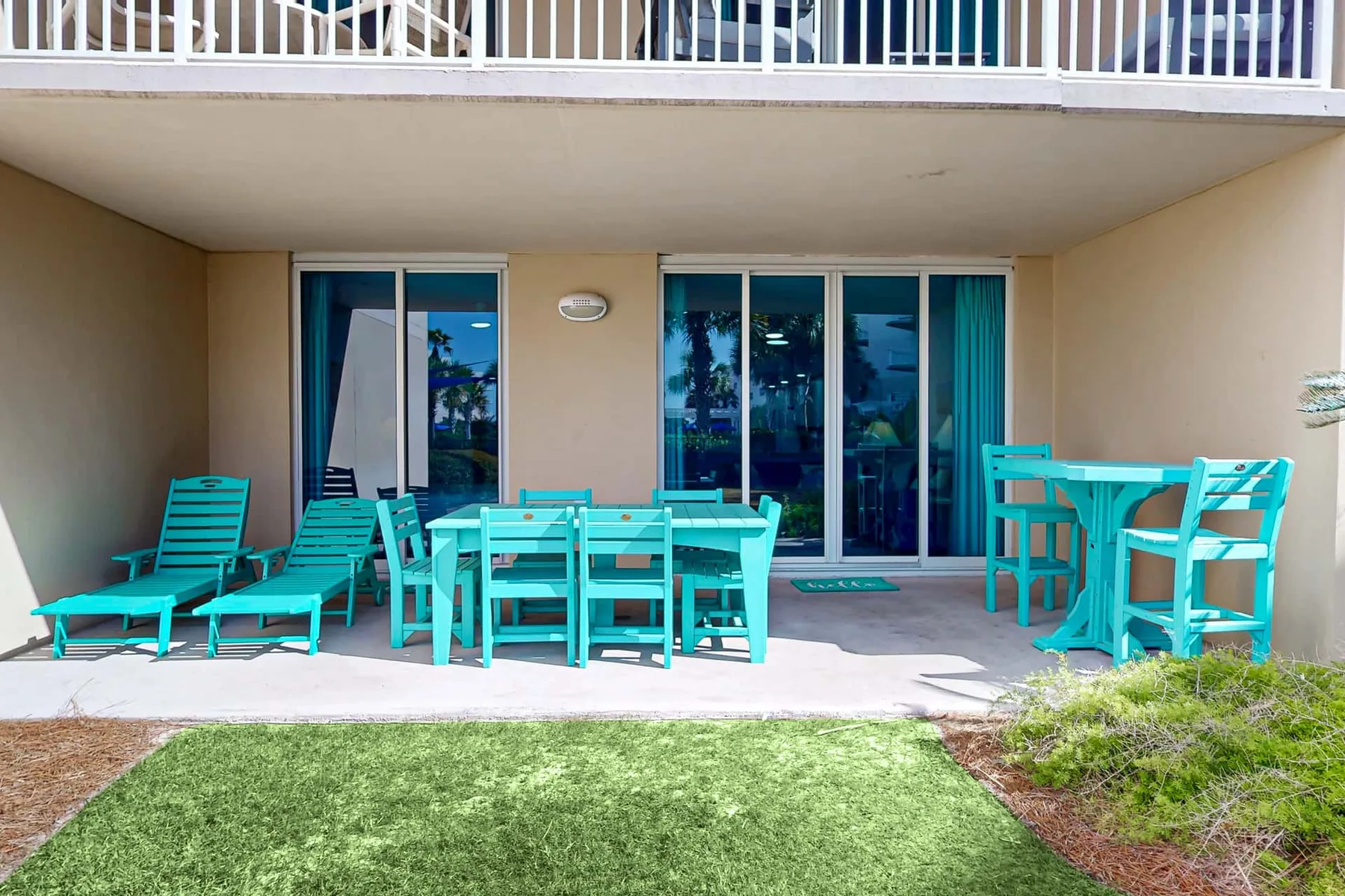 A covered patio with turquoise seating and a dining table faces sliding glass doors.