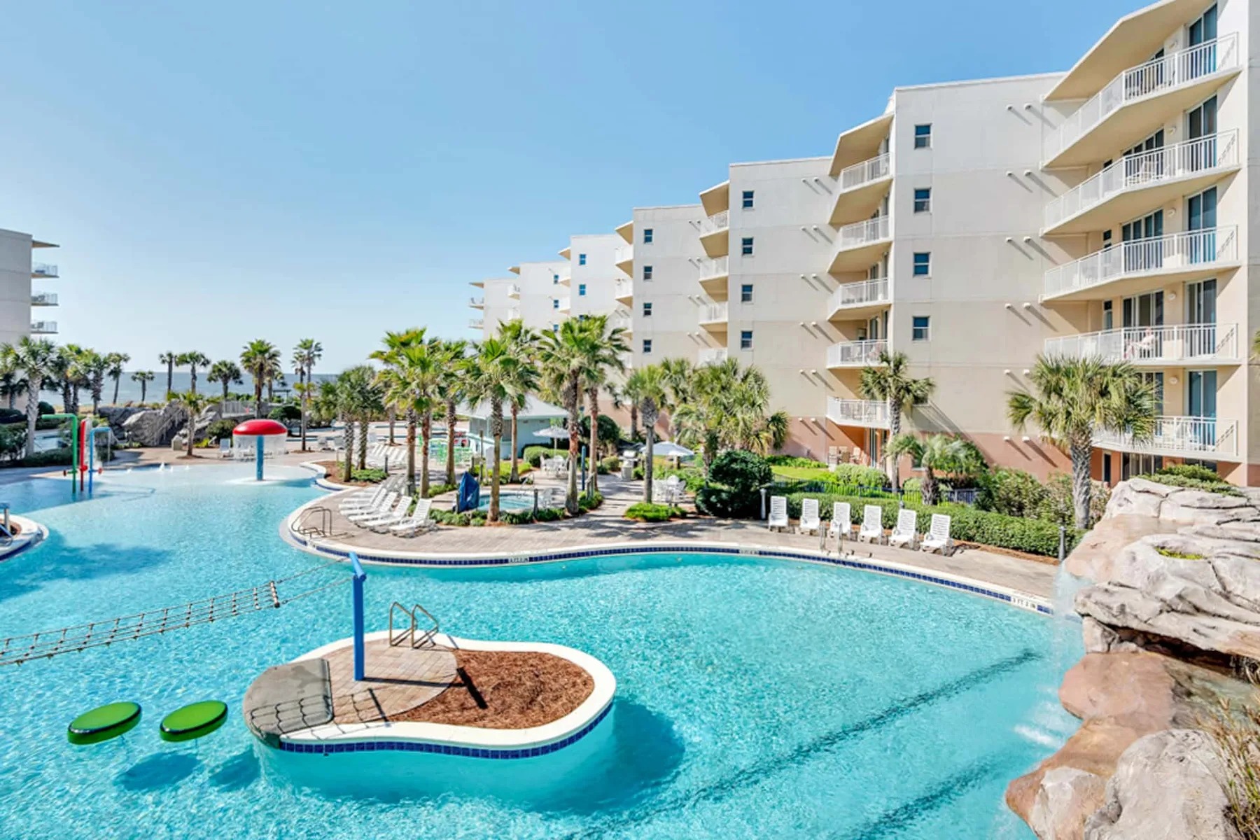 A resort pool with palm trees and white buildings in the background.