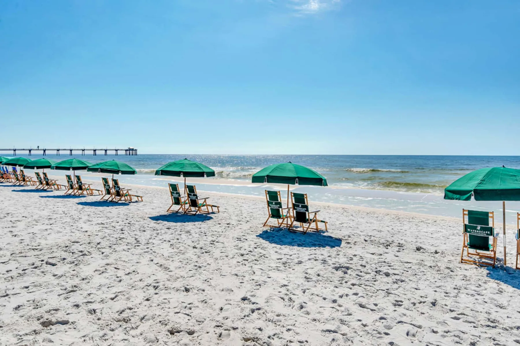 A sandy beach with green umbrellas and chairs beside the ocean.