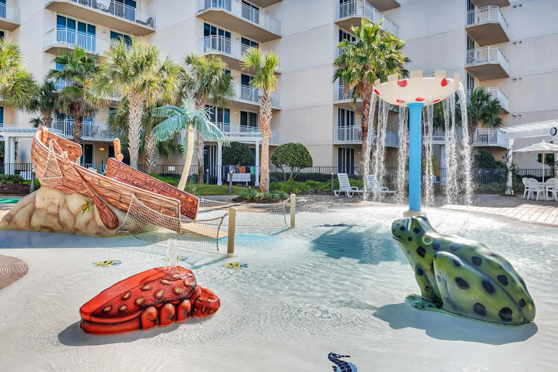 A shallow pool features a colorful play area with a frog sculpture and water sprays.