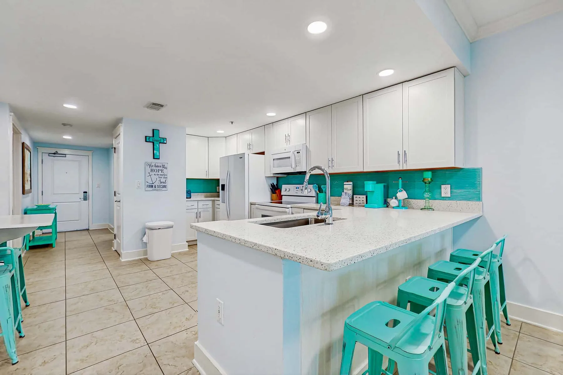 A bright kitchen with white cabinets, a turquoise backsplash, and counter seating.
