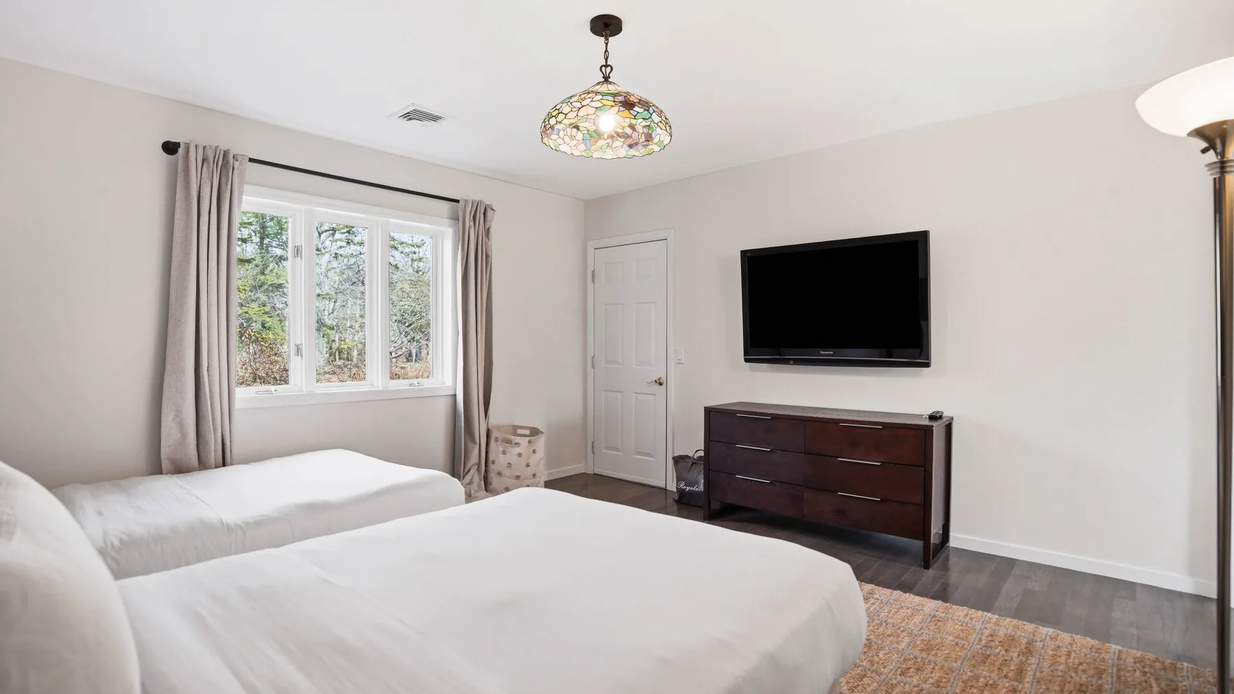 Un dormitorio con dos camas, una ventana y un televisor sobre una cómoda.