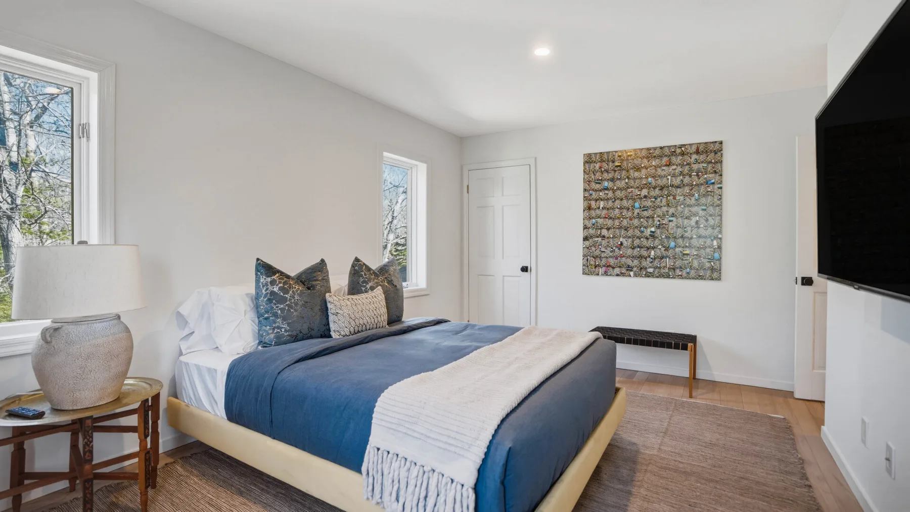 Un dormitorio luminoso con una cama vestida con ropa de cama azul y un televisor en la pared.