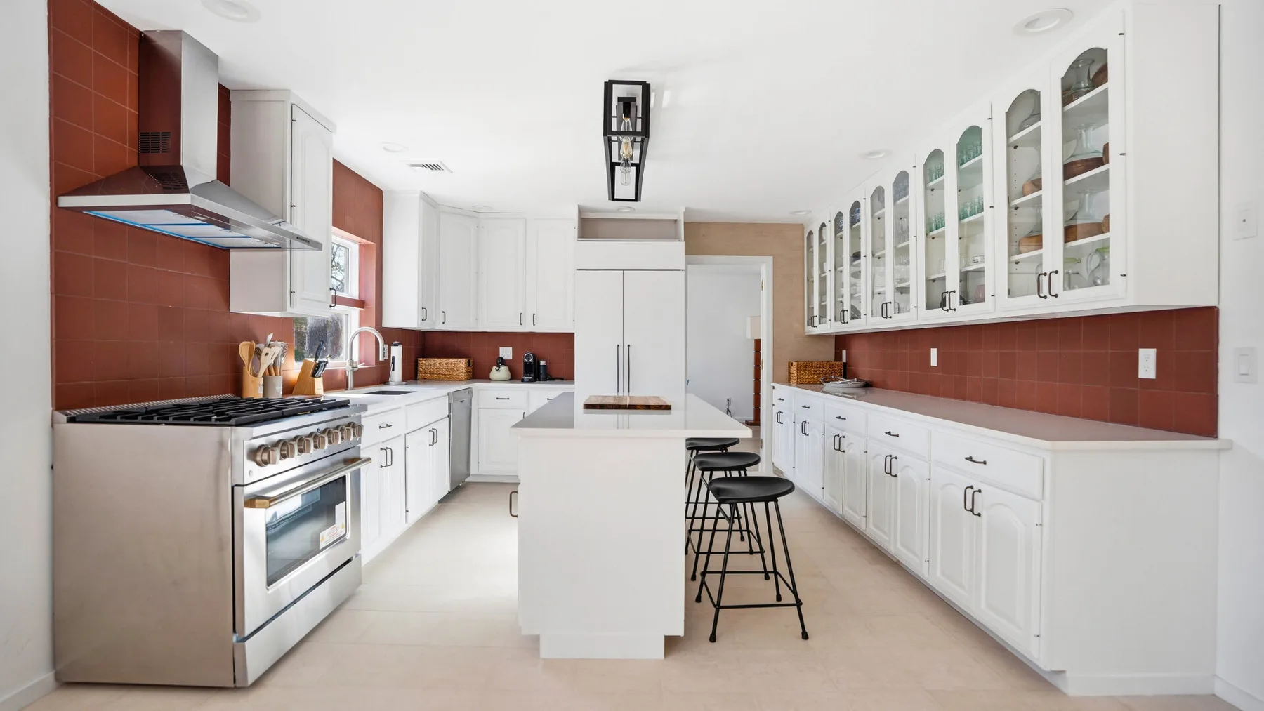 Una cocina luminosa con gabinetes blancos, salpicadero de azulejos rojos e isla central.