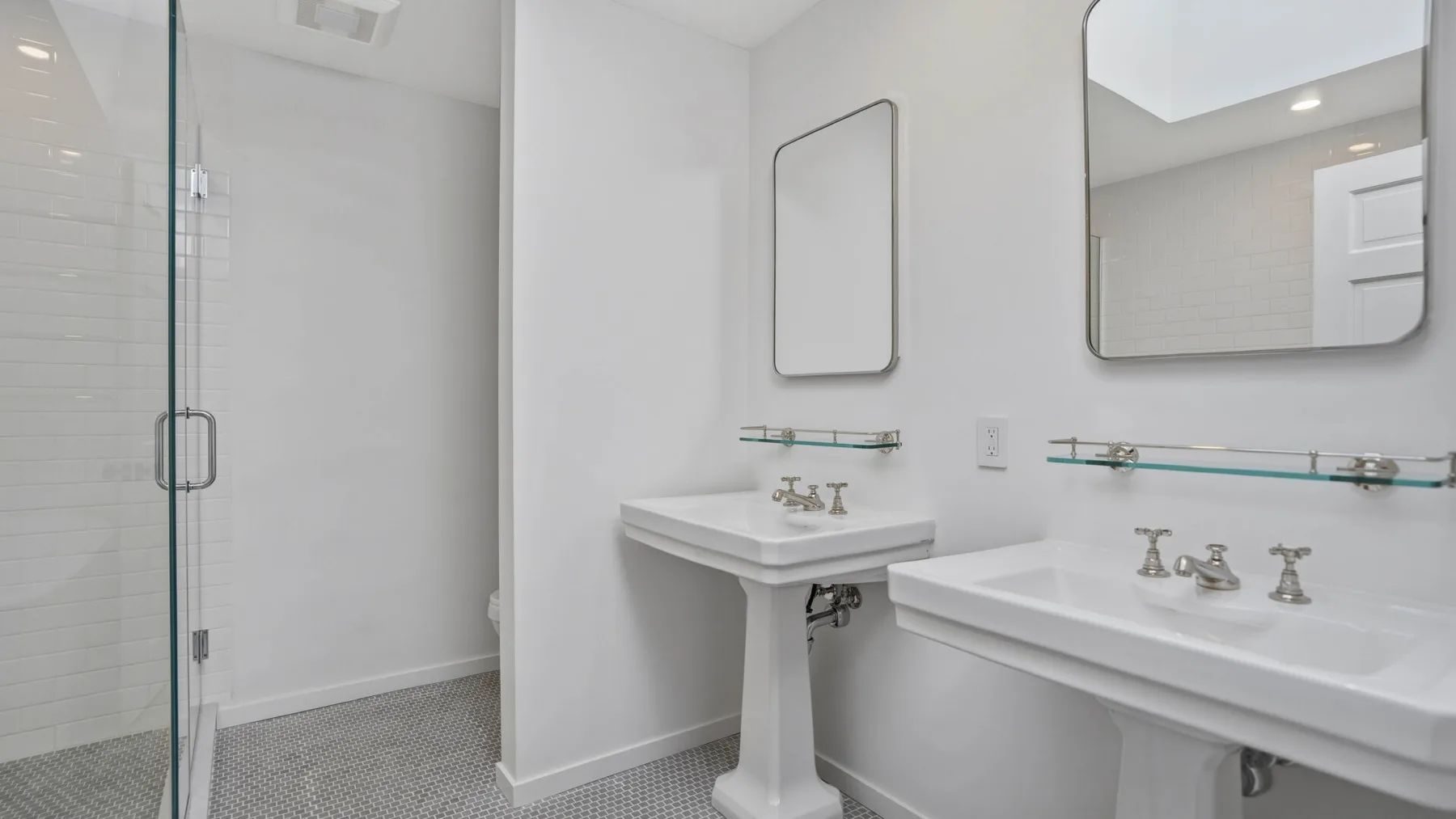 Un baño luminoso con ducha de vidrio y lavabos de pedestal.