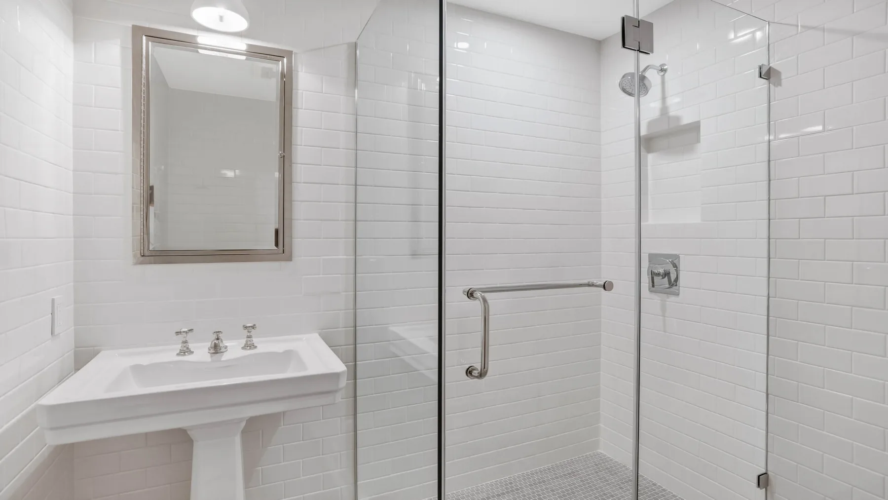 Un baño luminoso con azulejos, lavabo de pedestal y ducha de vidrio.