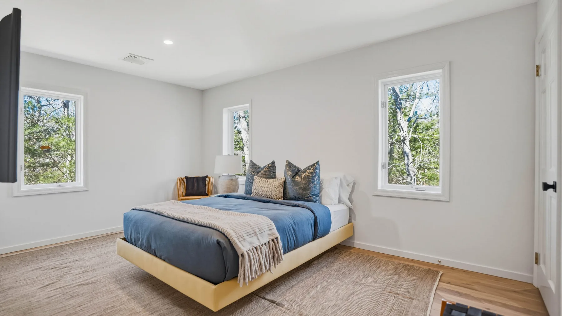Un dormitorio luminoso con una cama tendida y ventanas con vistas a la vegetación.