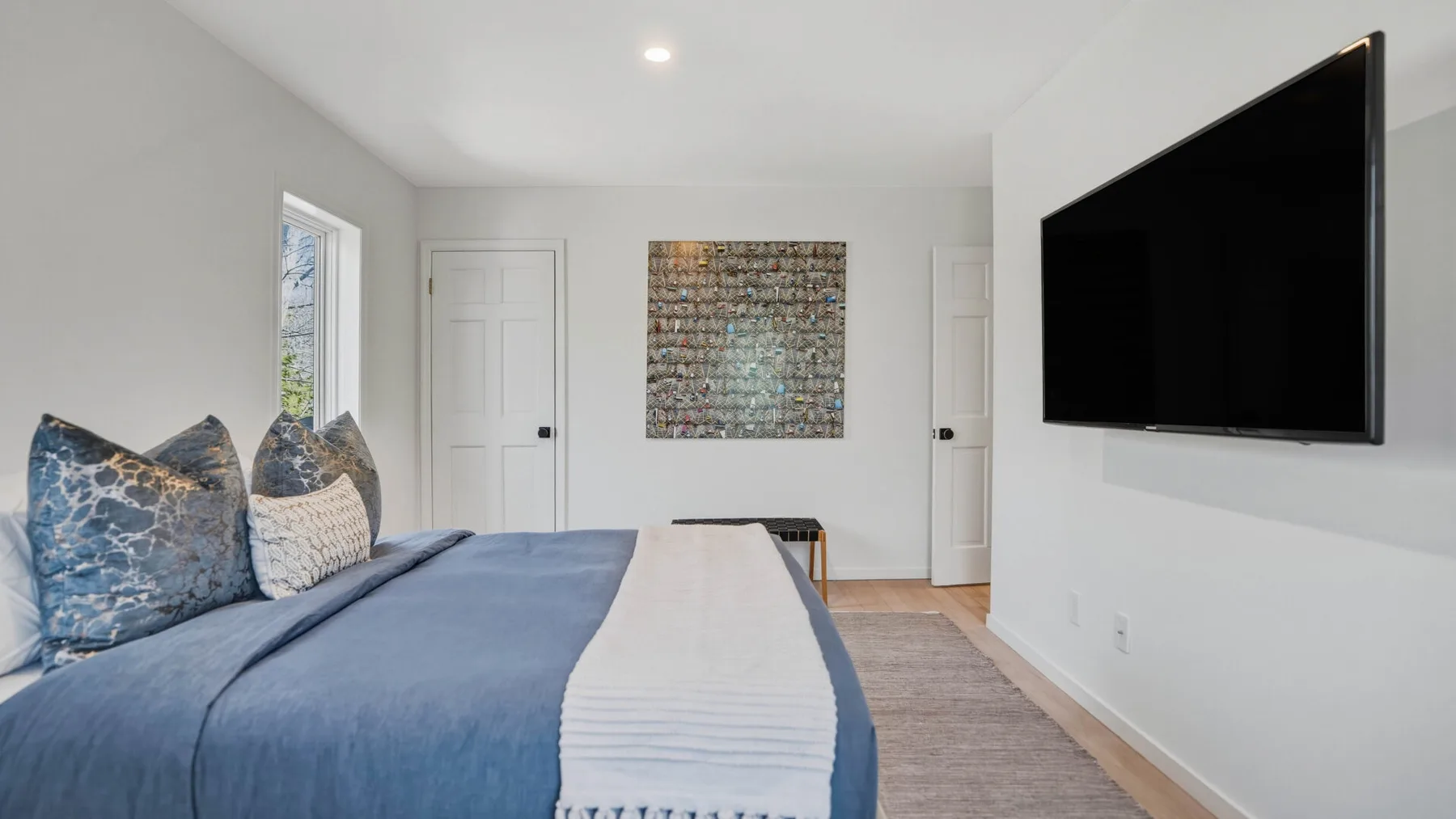 Un dormitorio con una cama, un televisor montado en la pared y una obra enmarcada.