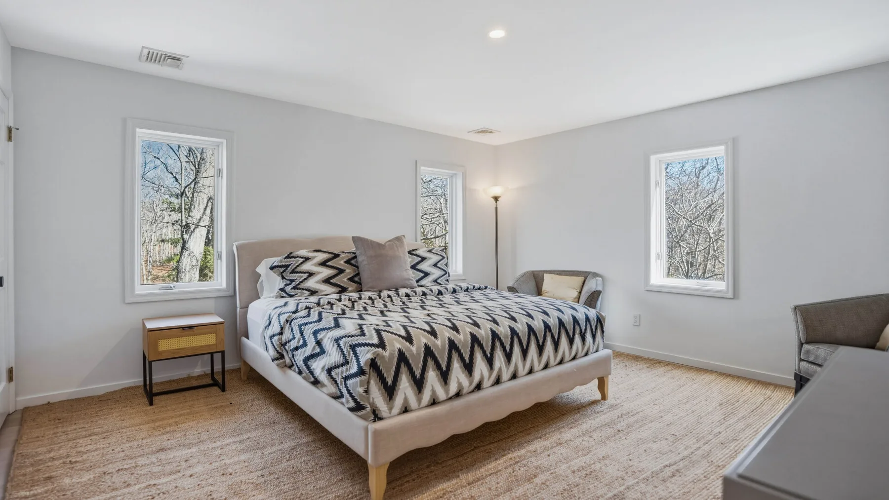 Un dormitorio luminoso con una colcha estampada y ventanas con vista a los árboles.