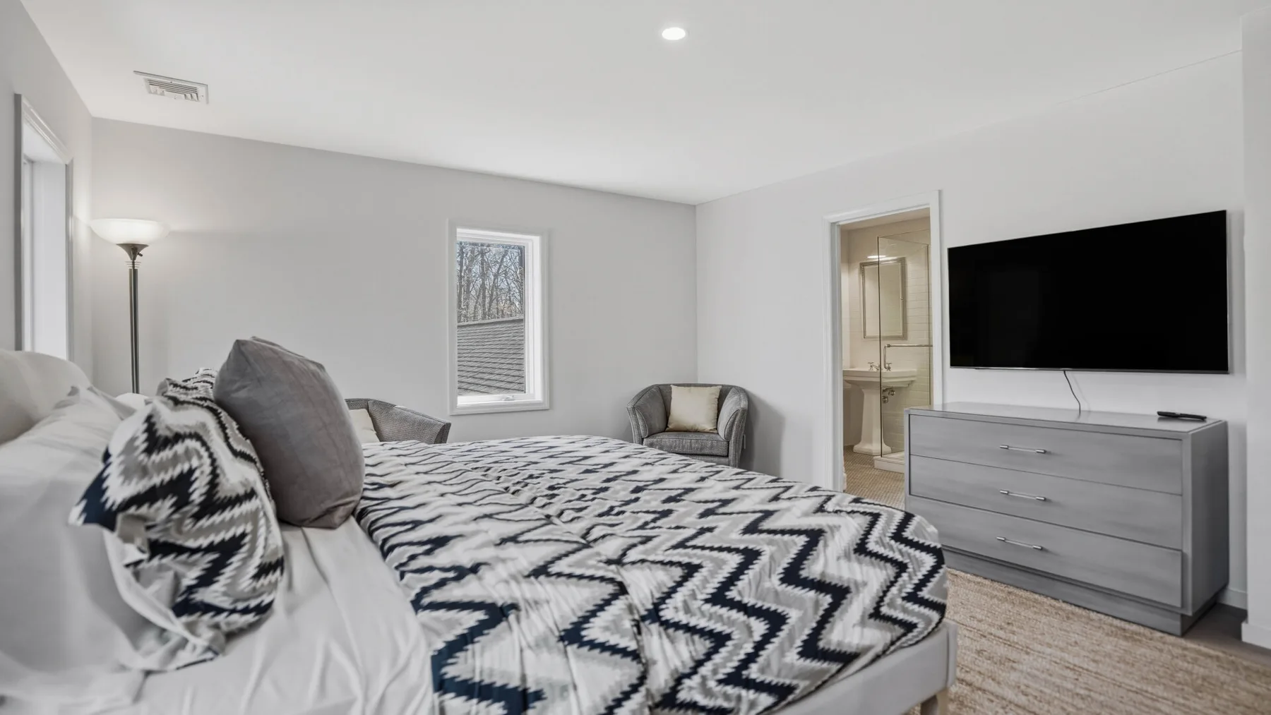 Un dormitorio con una cama, ropa de cama estampada y un televisor sobre una cómoda.