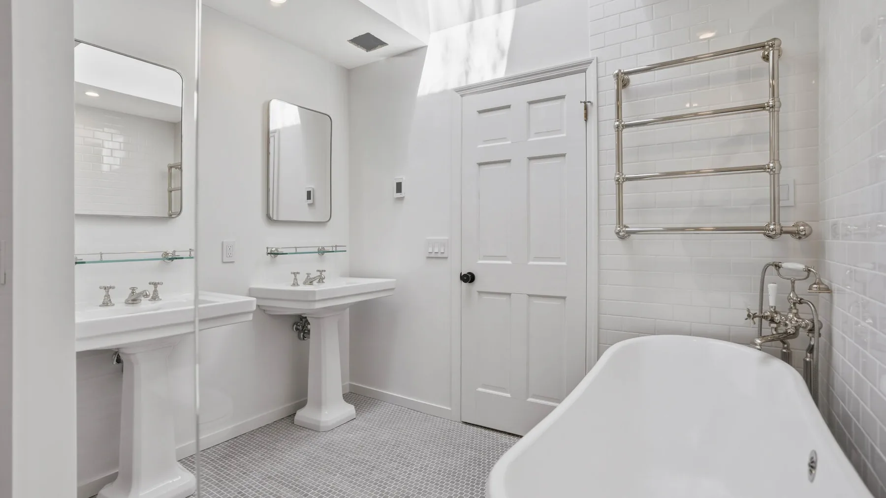 Un baño luminoso con lavabos de pedestal y una bañera exenta.