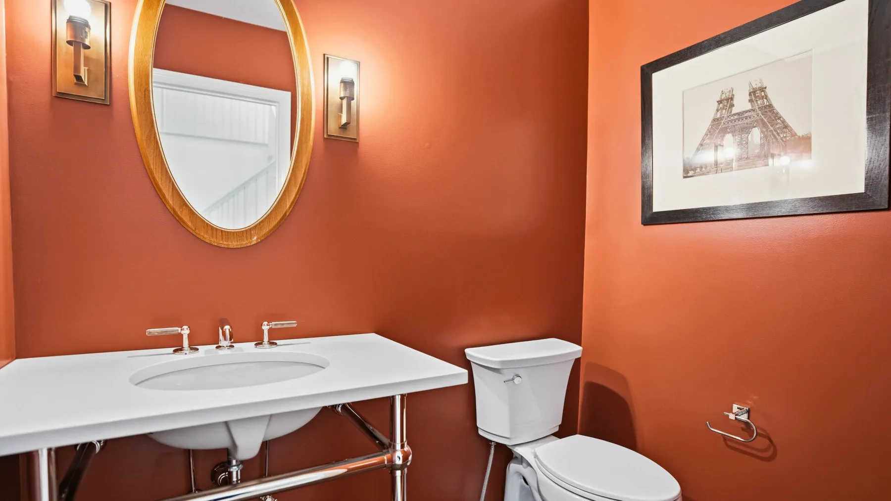 Un baño con lavabo blanco, inodoro y espejo ovalado en la pared.