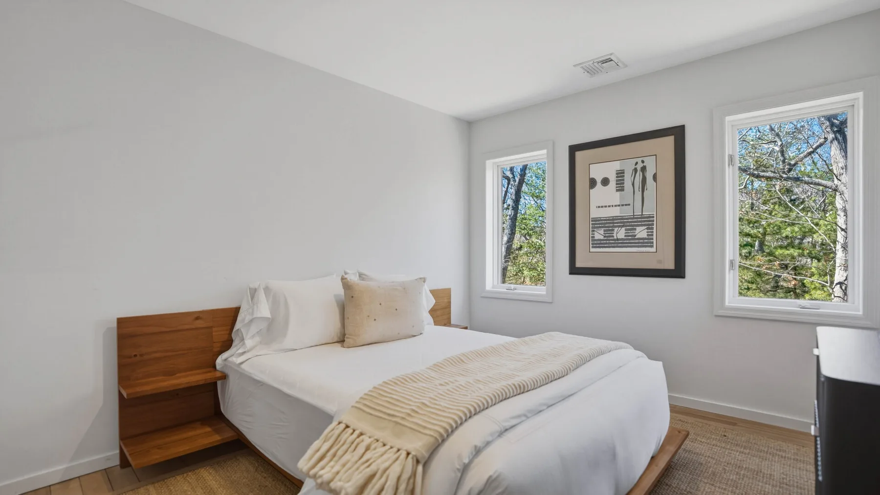 Un dormitorio luminoso con una cama, ropa de cama clara y arte enmarcado.