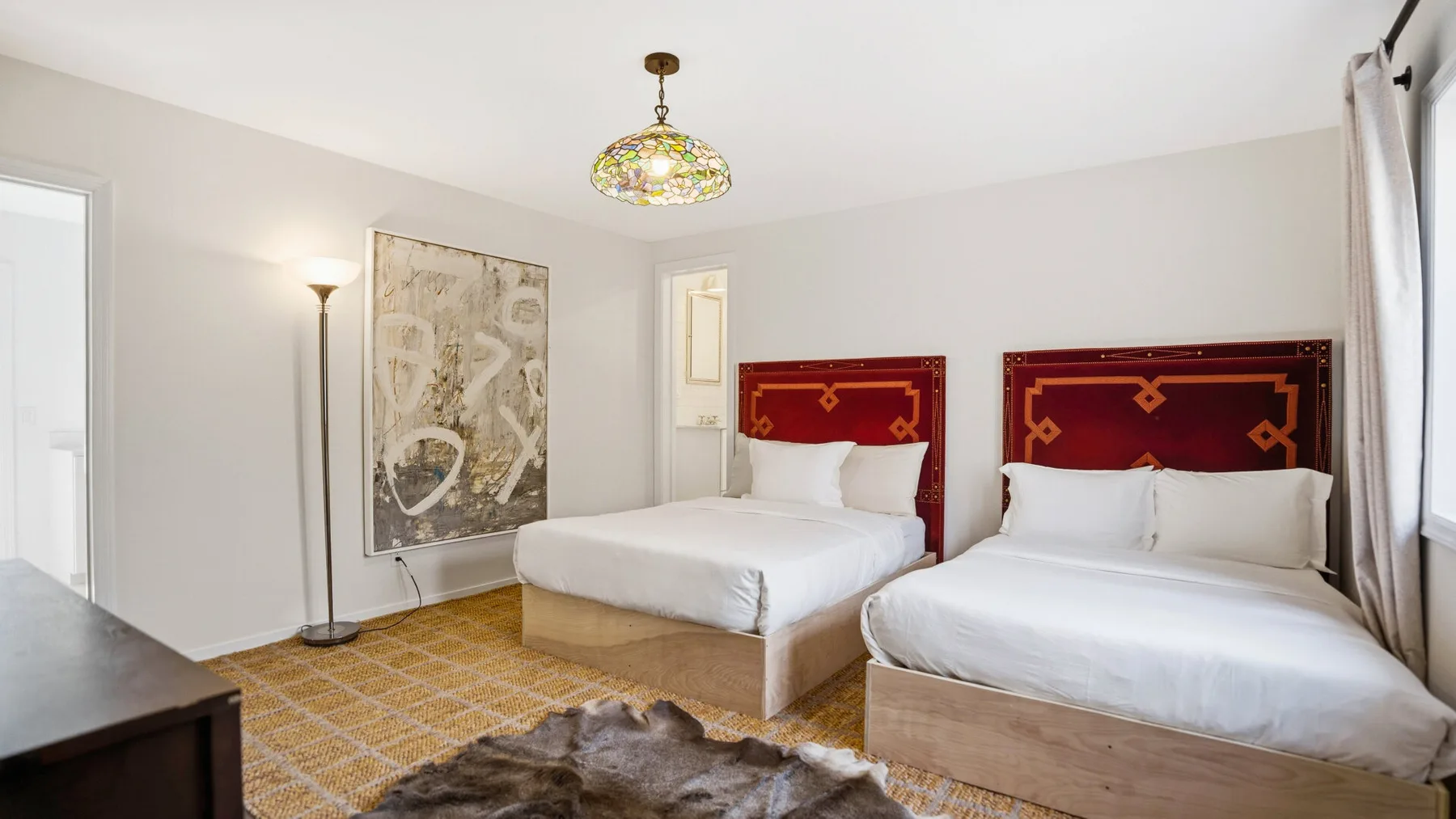 Un dormitorio luminoso con dos camas, cabeceros estampados y una alfombra.