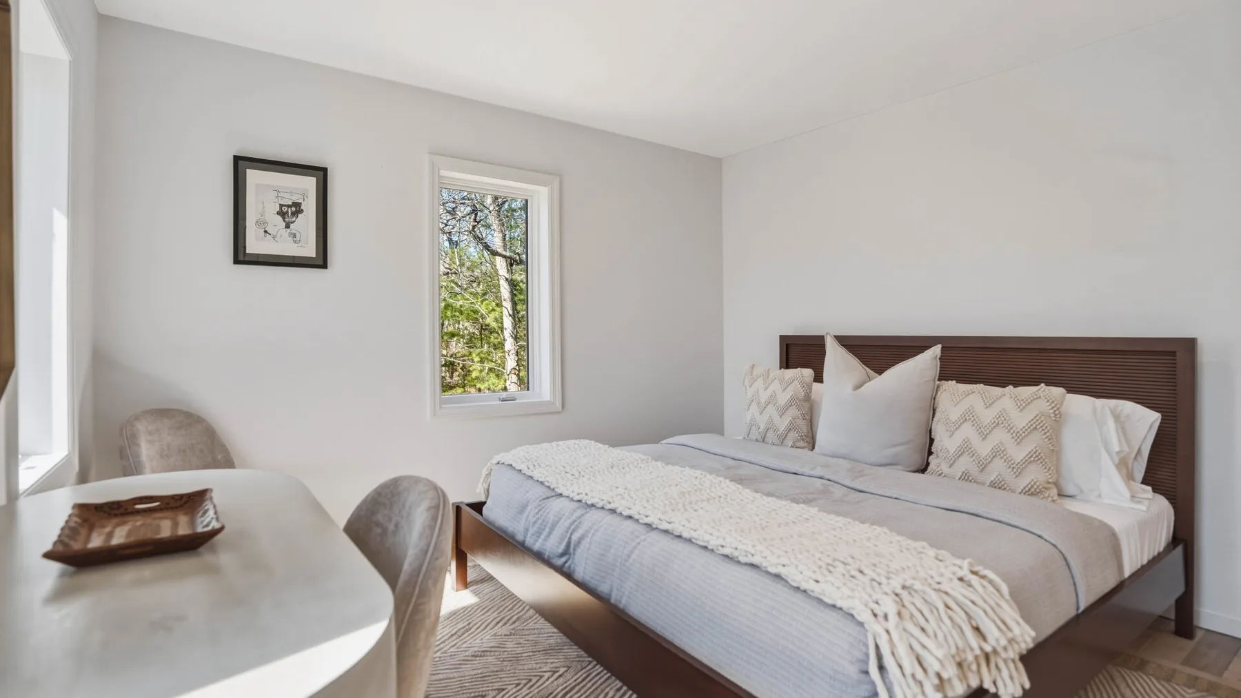 Un dormitorio con una cama vestida con ropa de cama clara y una pequeña zona para sentarse.