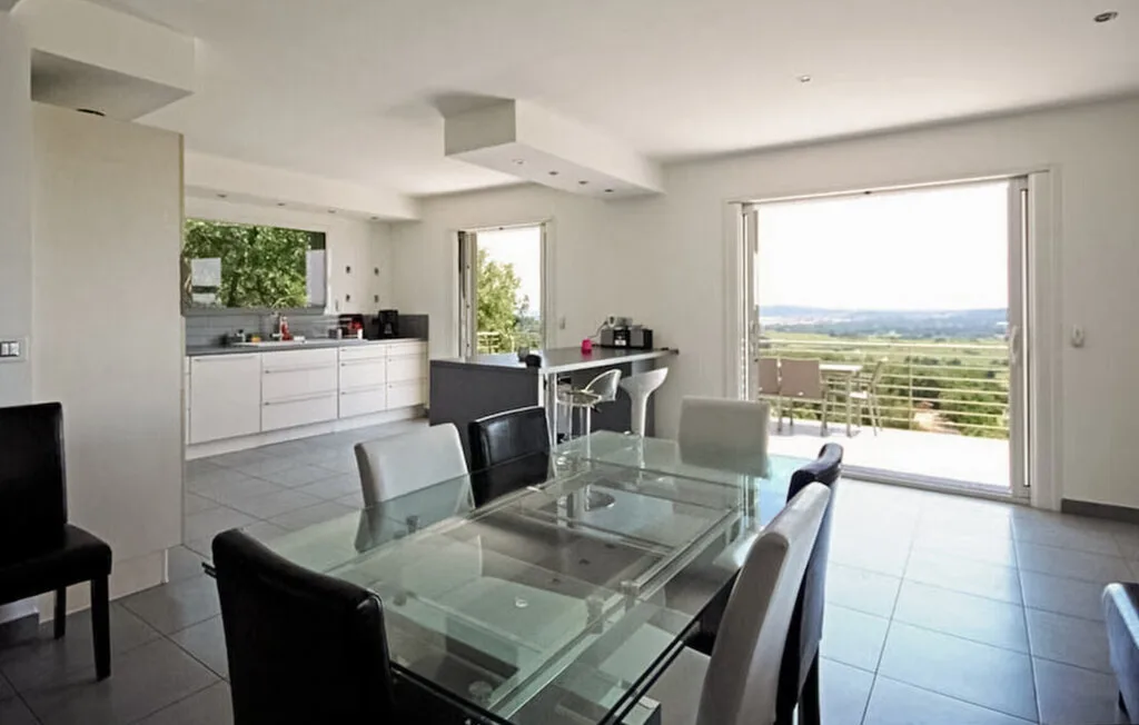 A bright dining area with a glass table opens onto a balcony with a wide view.