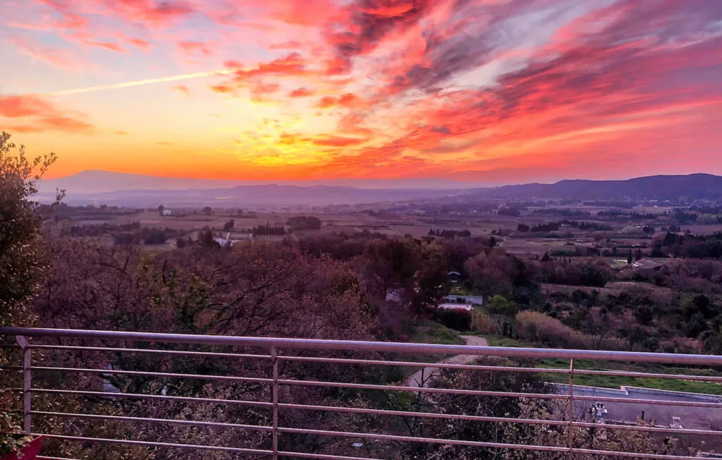 El cielo al atardecer ilumina un amplio valle, visto detrás de una barandilla.