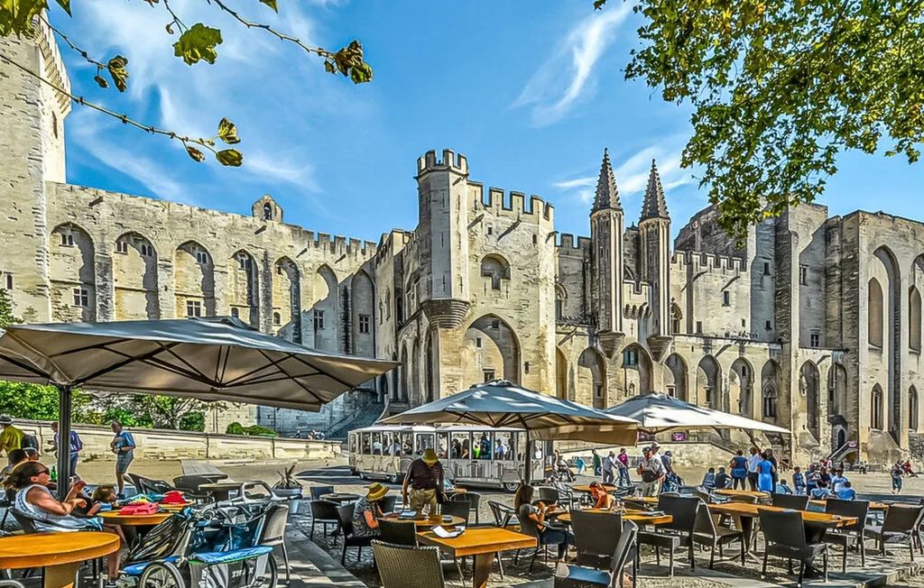 Una terraza de café al aire libre con mesas y asientos frente a un edificio histórico de piedra.