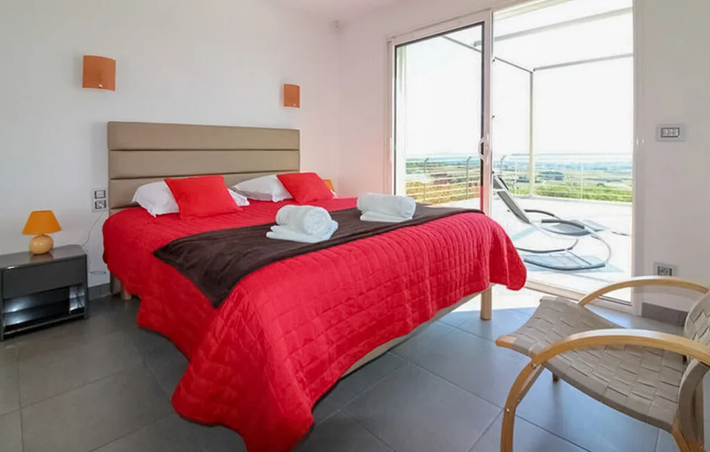 Un dormitorio con una cama cubierta de rojo junto a una puerta de cristal que da a un balcón.