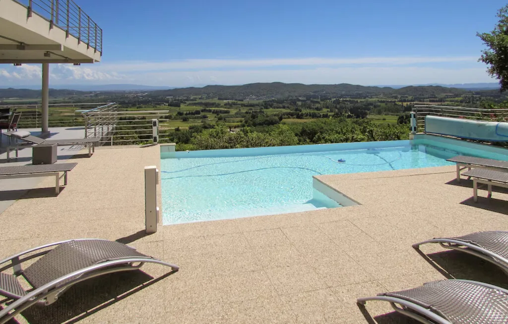 Una piscina al aire libre tiene vistas a un paisaje verde y colinas lejanas.