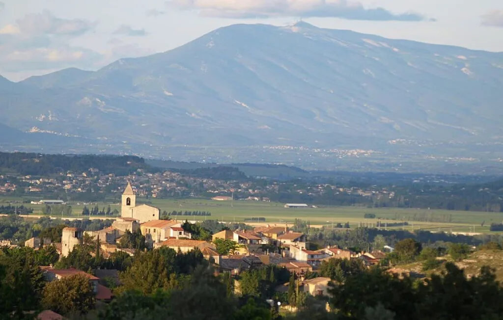 Un pequeño pueblo se encuentra entre colinas verdes, con una amplia montaña al fondo.