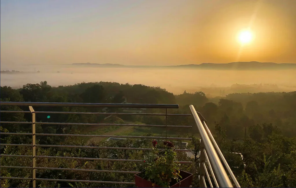 Una barandilla de terraza da a un paisaje arbolado bajo la luz dorada de la mañana.