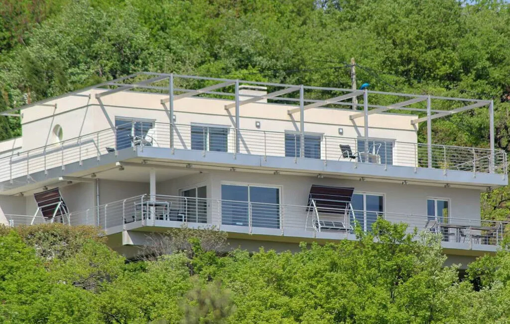 Un edificio moderno de varios niveles con amplios balcones se alza entre árboles frondosos.