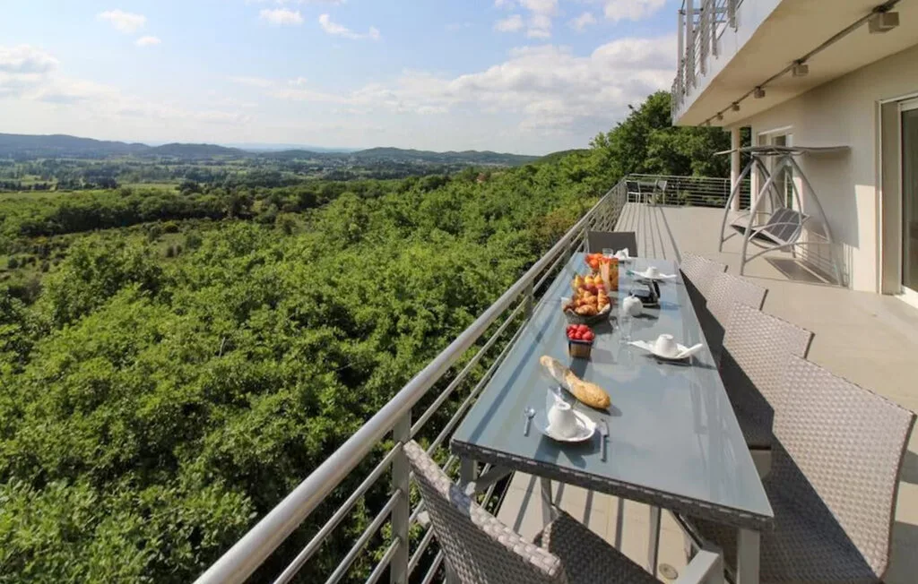 An outdoor dining terrace overlooks a broad expanse of green countryside.