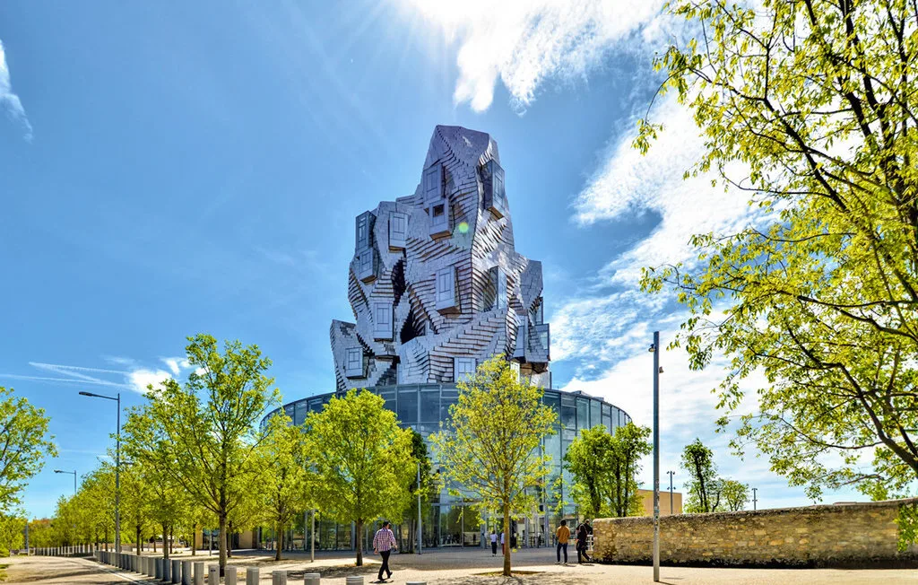 Un llamativo edificio moderno se eleva sobre una plaza arbolada.