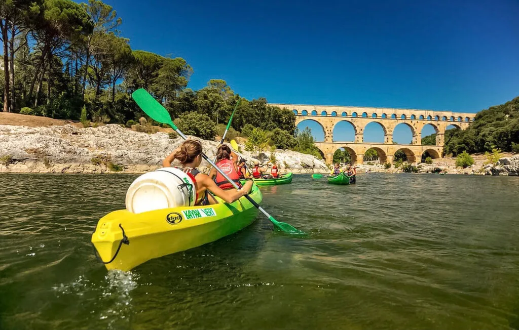 Varias personas reman en un kayak amarillo por un río bajo un acueducto de piedra.